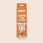 A tall rectangular package of dokitti Canine Yak Chew dog treats on a plain warm beige background. The box is orange with white text, a small dog photo near the bottom, and product details including 'Peanut Butter' and size markings.